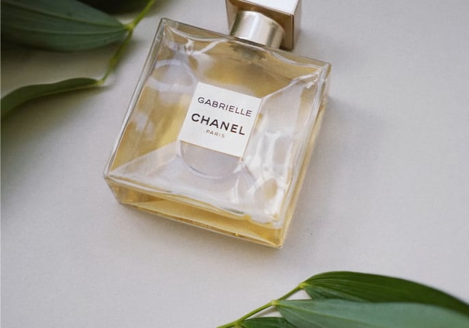 photo of Gabrielle Essence Eau De Parfume lying on a flat surface. Green leaves peak into the photo from the left upper corner and right bottom corner